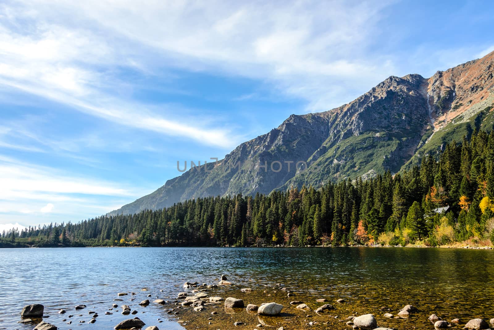 Beautiful autumn mountain landscape with a lake and a forest at the foot of rocky mountains against the blue sky