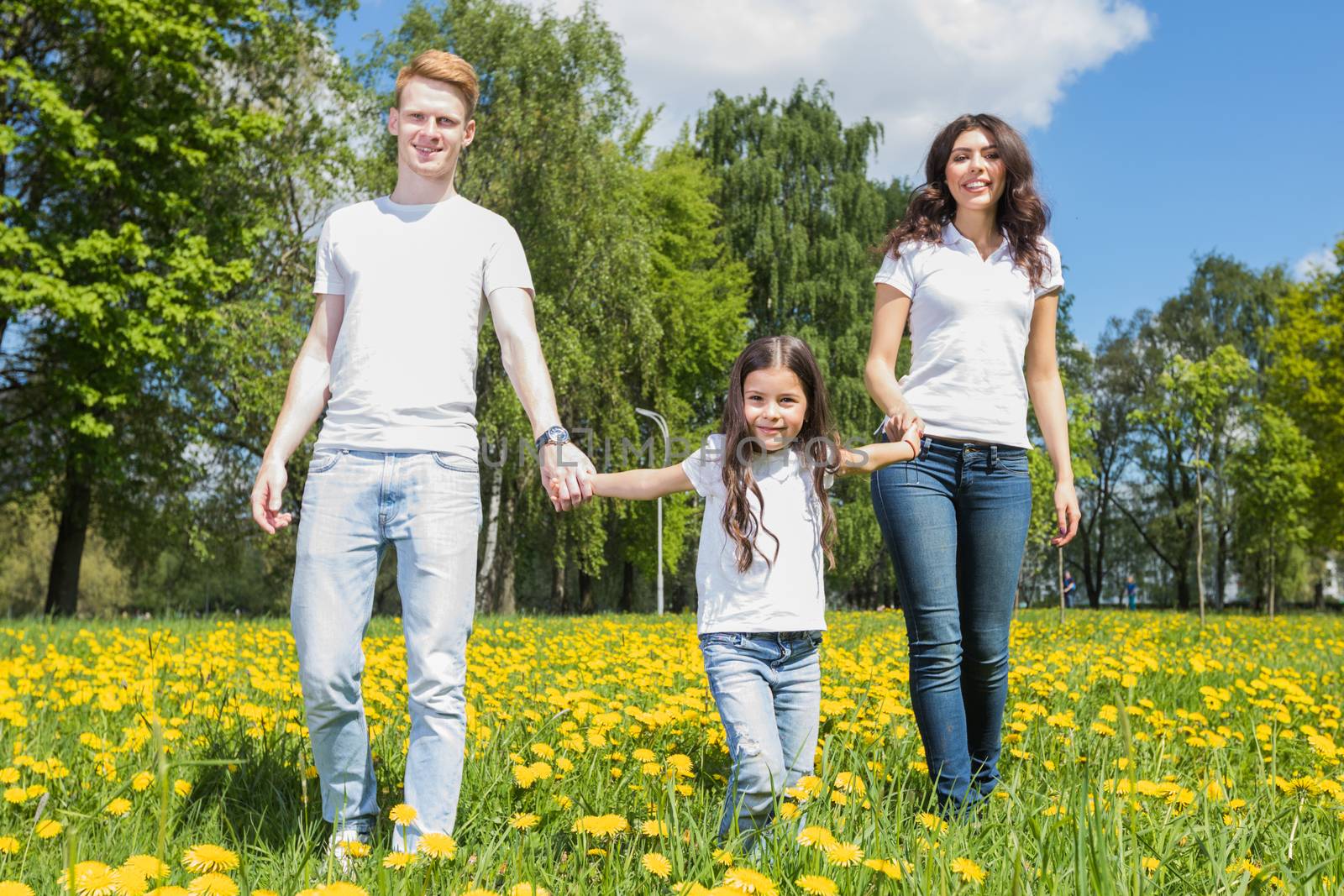 Family of three walking on spring meadow of blooming yellow dandelion flowers being happy