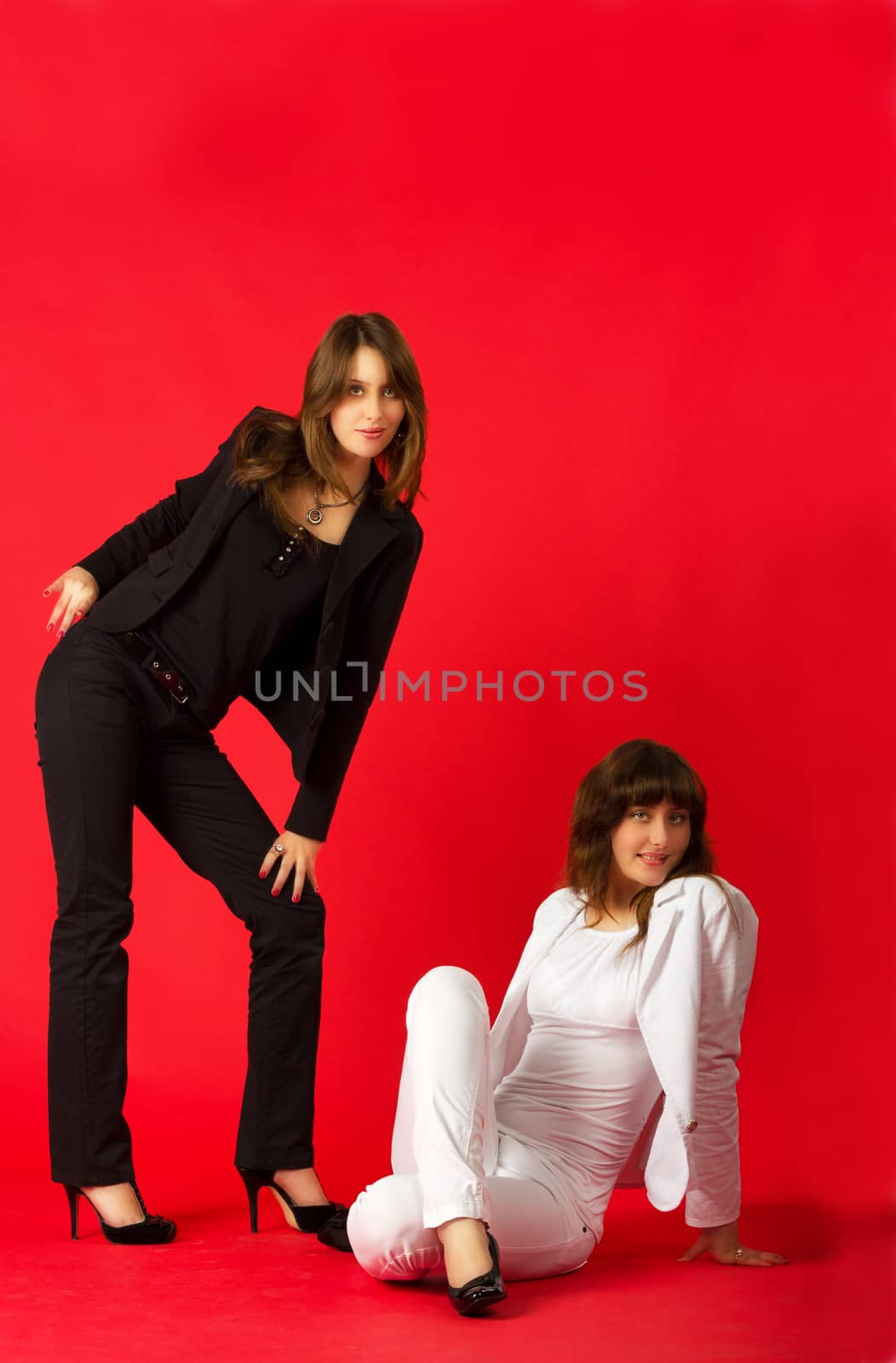 young pretty sisters twins posing in studio on red background