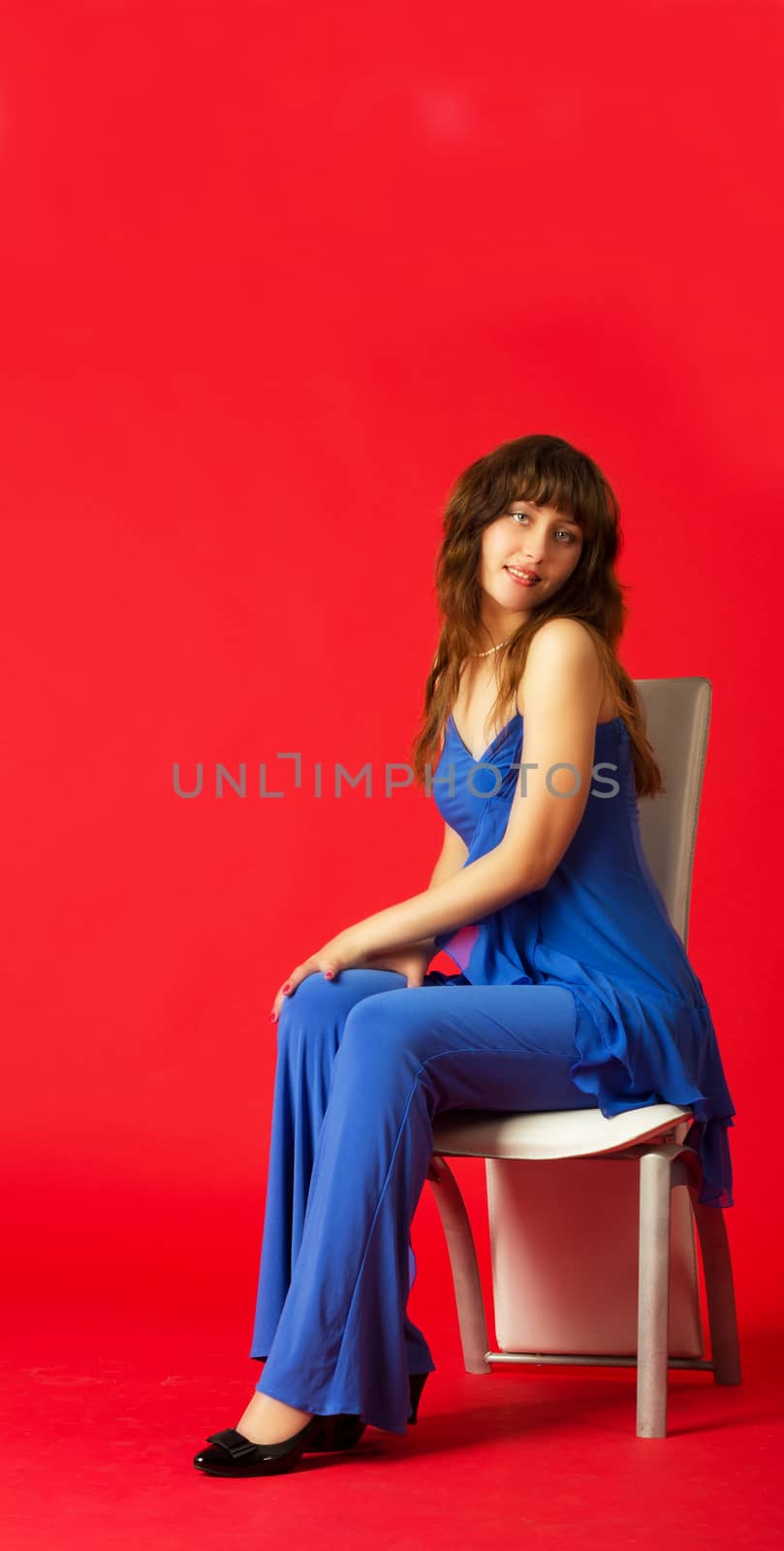 pretty young girl in blue costume posing sitting on red background in studio