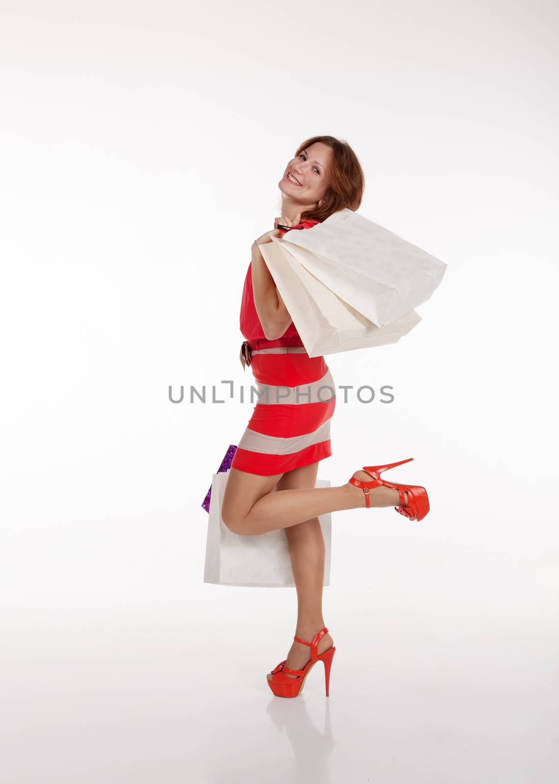 pretty smiling brunette woman in red dress and shoes standing with shopping bags
