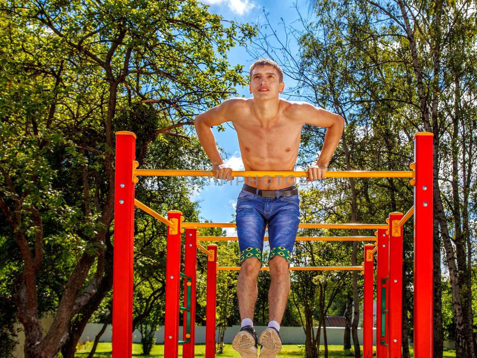 young man is practicing on a horizontal bar in the park on summer