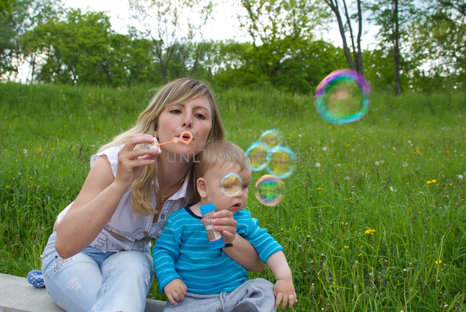 mother with her son blowing bubbles outside in city park on spring day