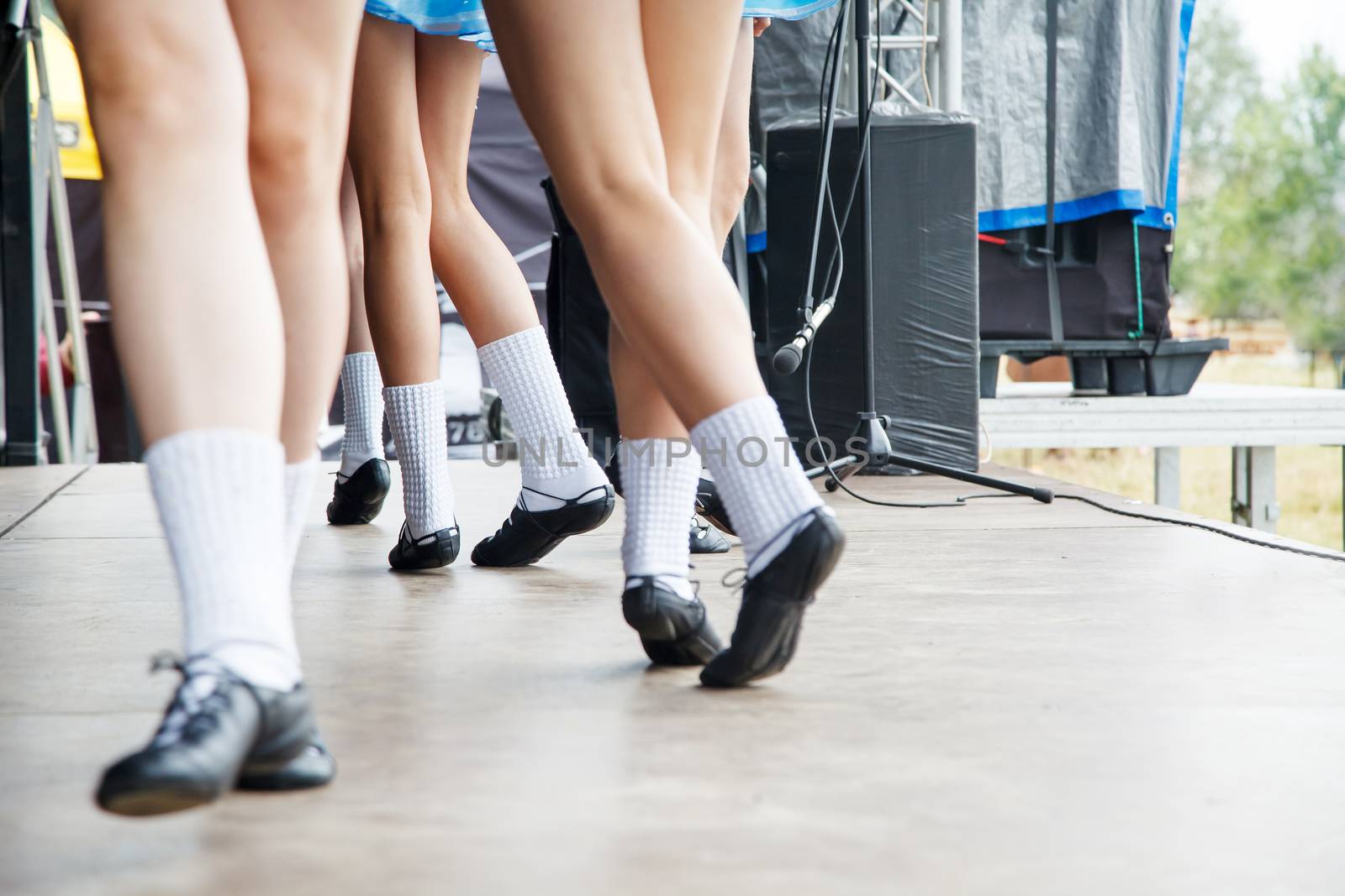 female legs of four irish dancers in blue dresses on the stage closeup