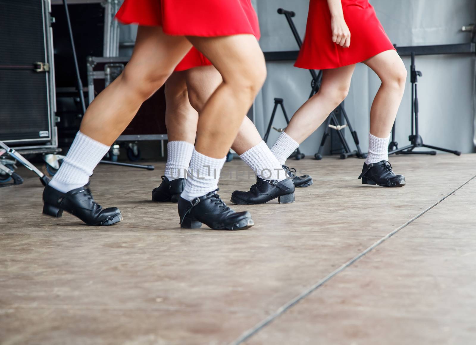 female legs of three irish dancers in red dresses on the stage