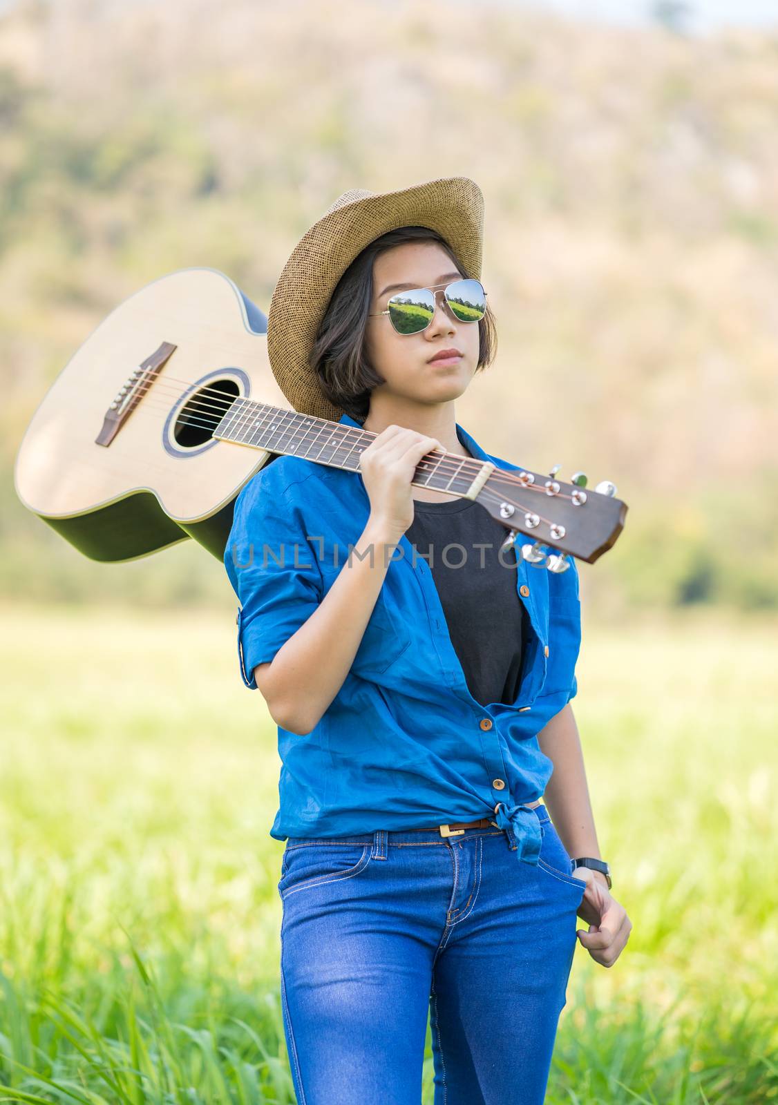 Woman wear hat and carry her guitar in grass field  by stoonn