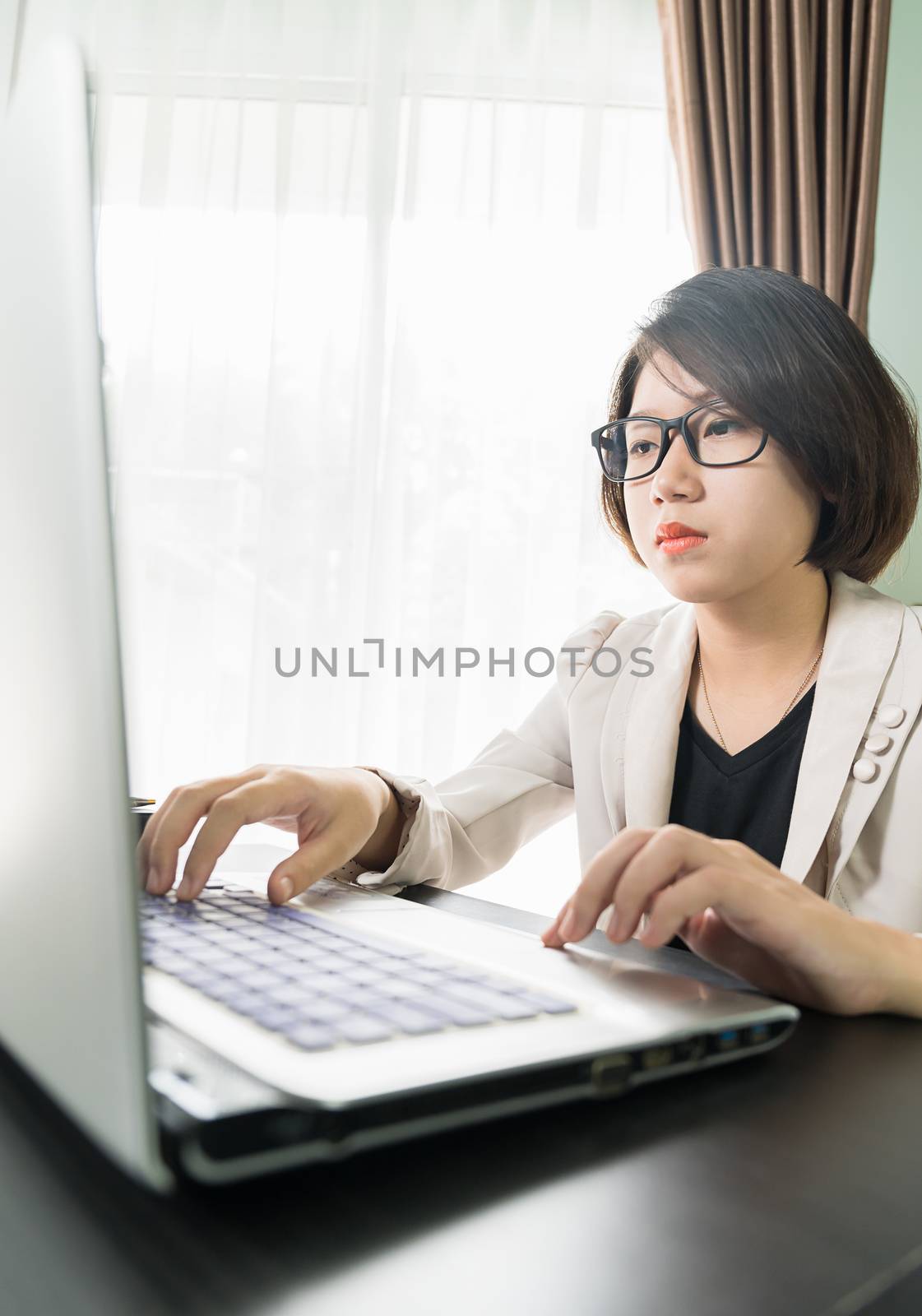 Woman teenage short hair in smart casual wear working on laptop while sit near window in home office