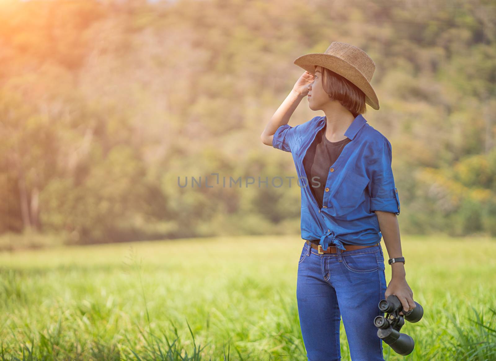 Young asian woman short hair wear hat and hold binocular in grass field countryside Thailand