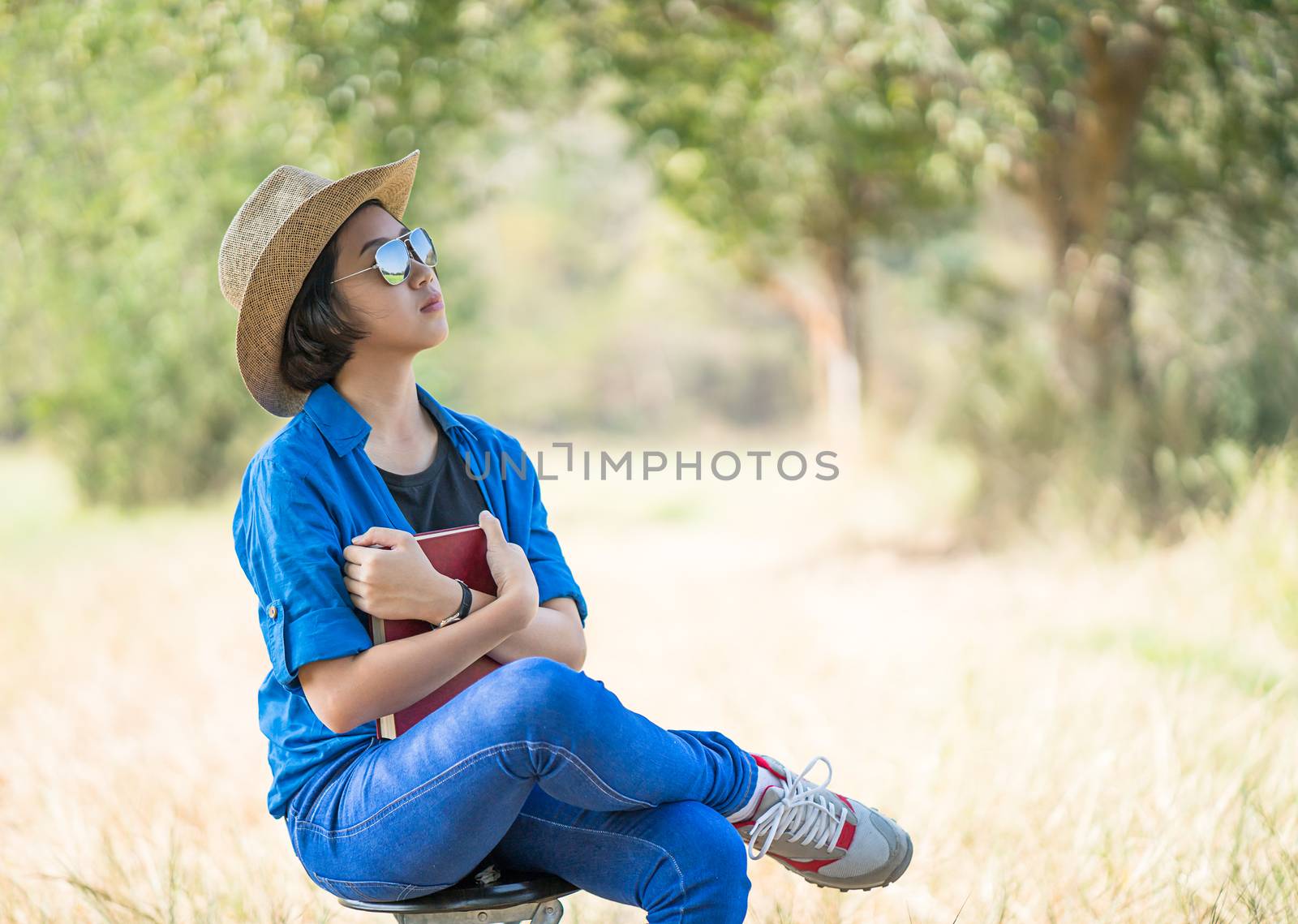 Young asian women short hair wear hat and sunglasses read a book ,sit on chair in countryside Thailand