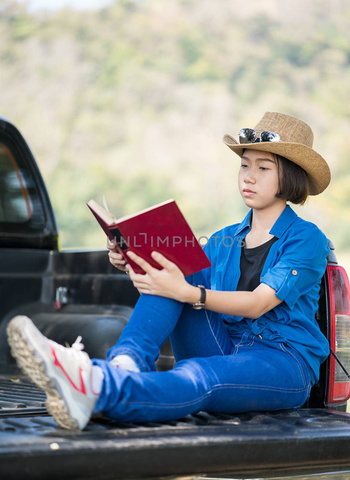 Young asian women short hair wear hat and sunglasses read a book ,sit on pickup truck in countryside Thailand