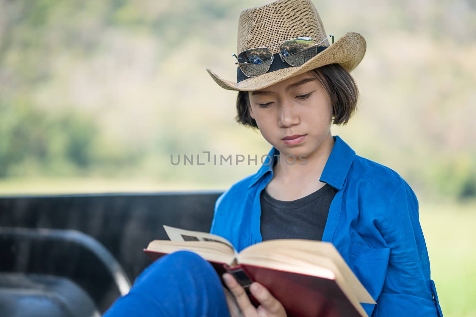 Young asian women short hair wear hat and sunglasses read a book ,sit on pickup truck in countryside Thailand