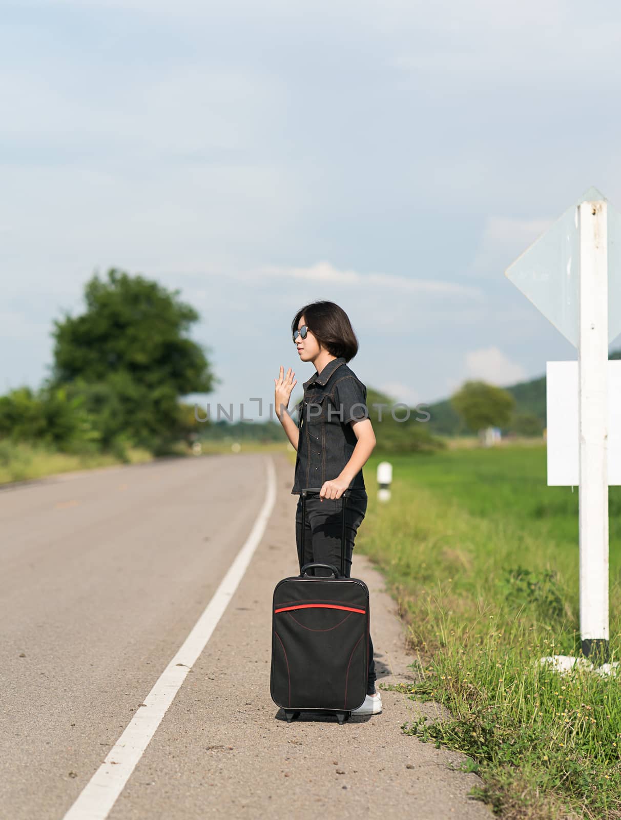 Woman with luggage hitchhiking along a road by stoonn