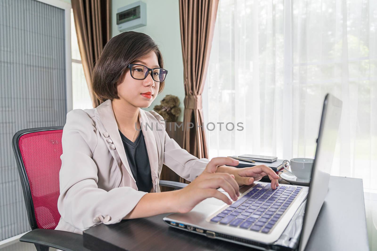 Young asian woman short hair in smart casual wear working on laptop while sitting near window in home office