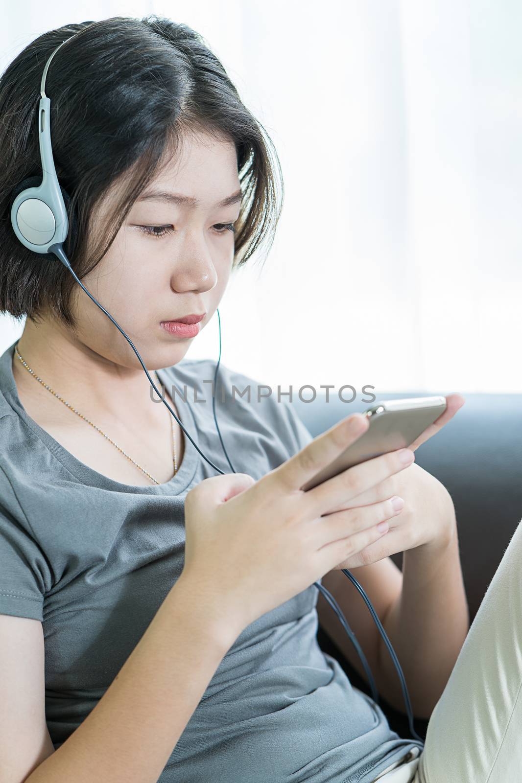 Close up young asian woman short hair listening music from mobile phone on the couch