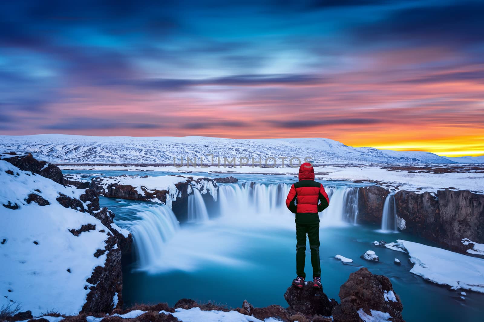Godafoss waterfall at sunset in winter, Iceland. Guy in red jacket looks at Godafoss waterfall. by gutarphotoghaphy
