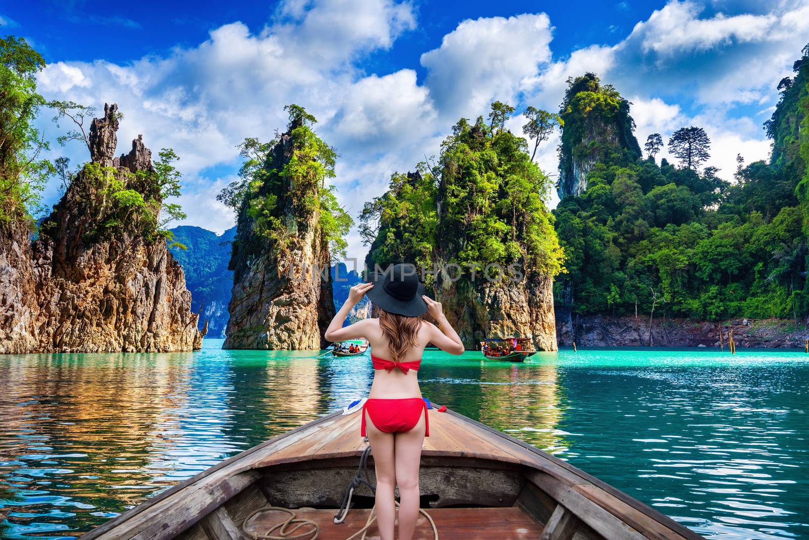 Beautiful girl standing on the boat and looking to mountains in Ratchaprapha Dam at Khao Sok National Park, Surat Thani Province, Thailand. by gutarphotoghaphy