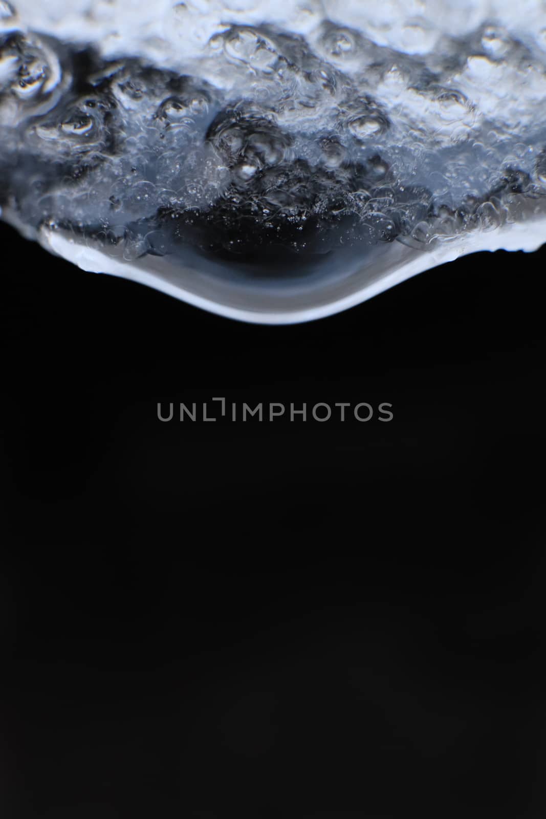 Handing down water drop from ice top. Cold clear rain drop with ice reflection inside. Macro closeup. by sanches812