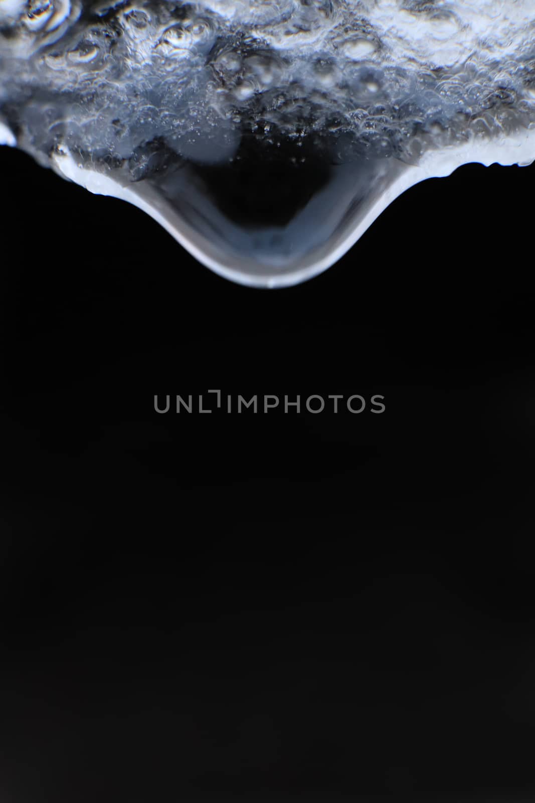 Cold clear rain drop with ice reflection inside. Handing down water drop from ice top on black background. Macro closeup.
