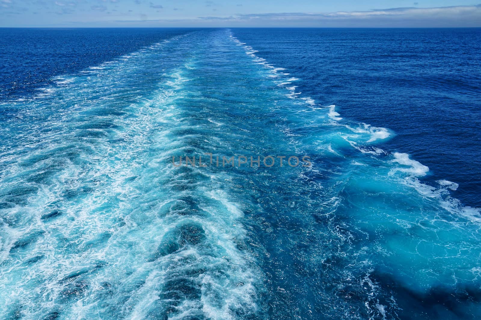 A Cruise ship wake on a beautiful sunny day with white clouds and blue seas on the Atlantic Ocean.