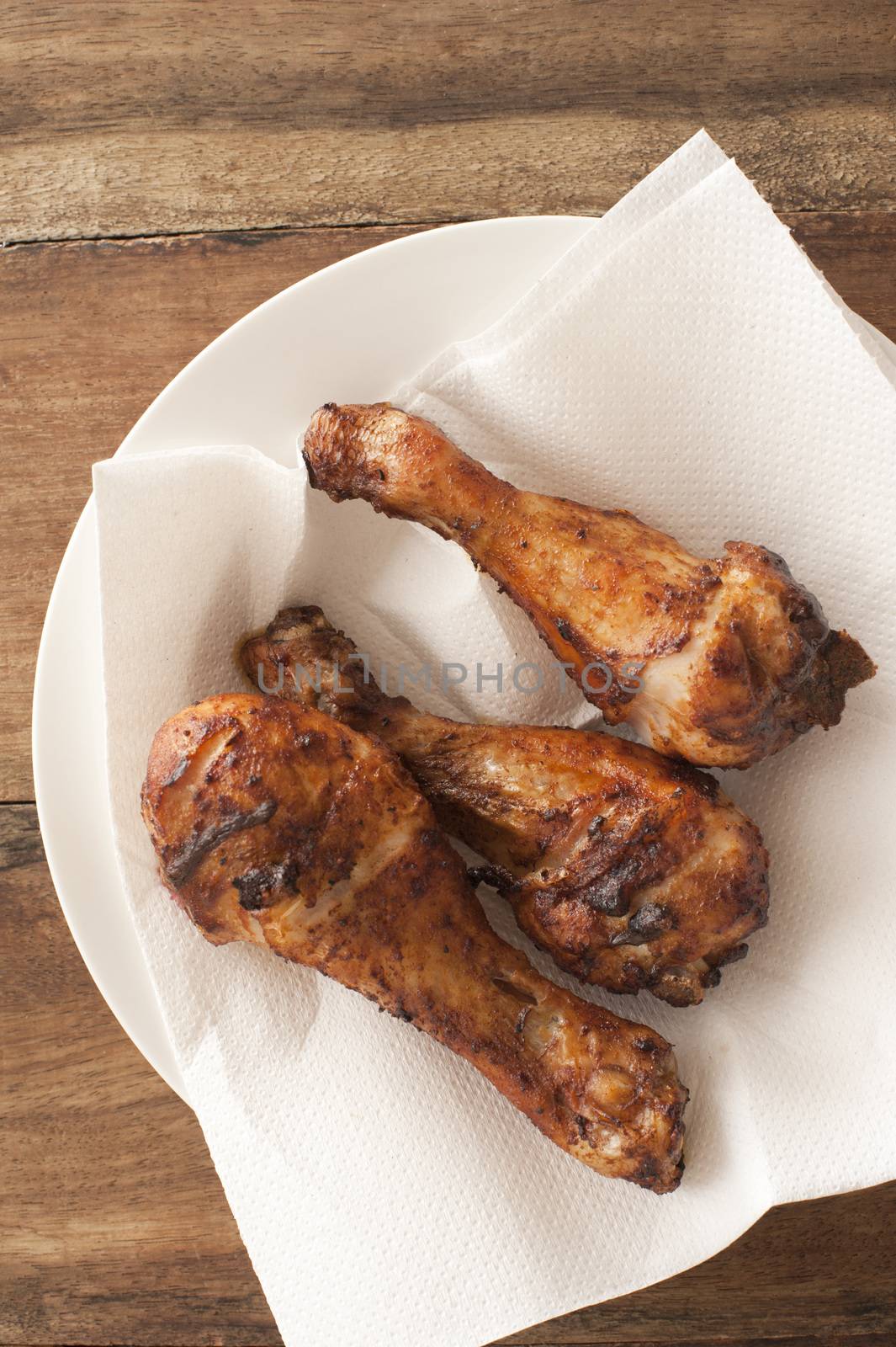 Three spicy grilled chicken legs served on a paper napkin on a plate for a tasty finger snack , overhead view on a wooden table