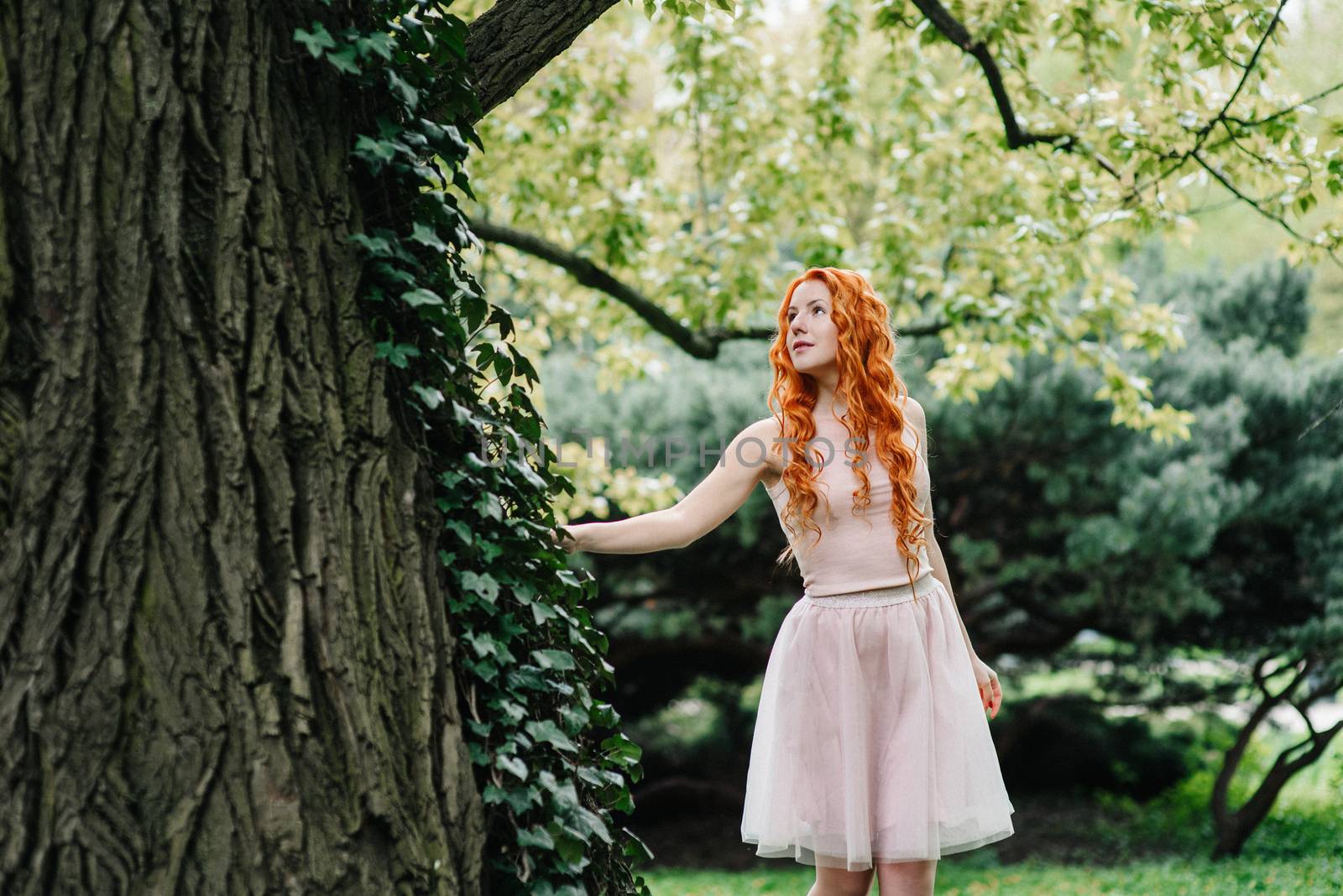 red-haired young girl walking in a park between trees by Andreua