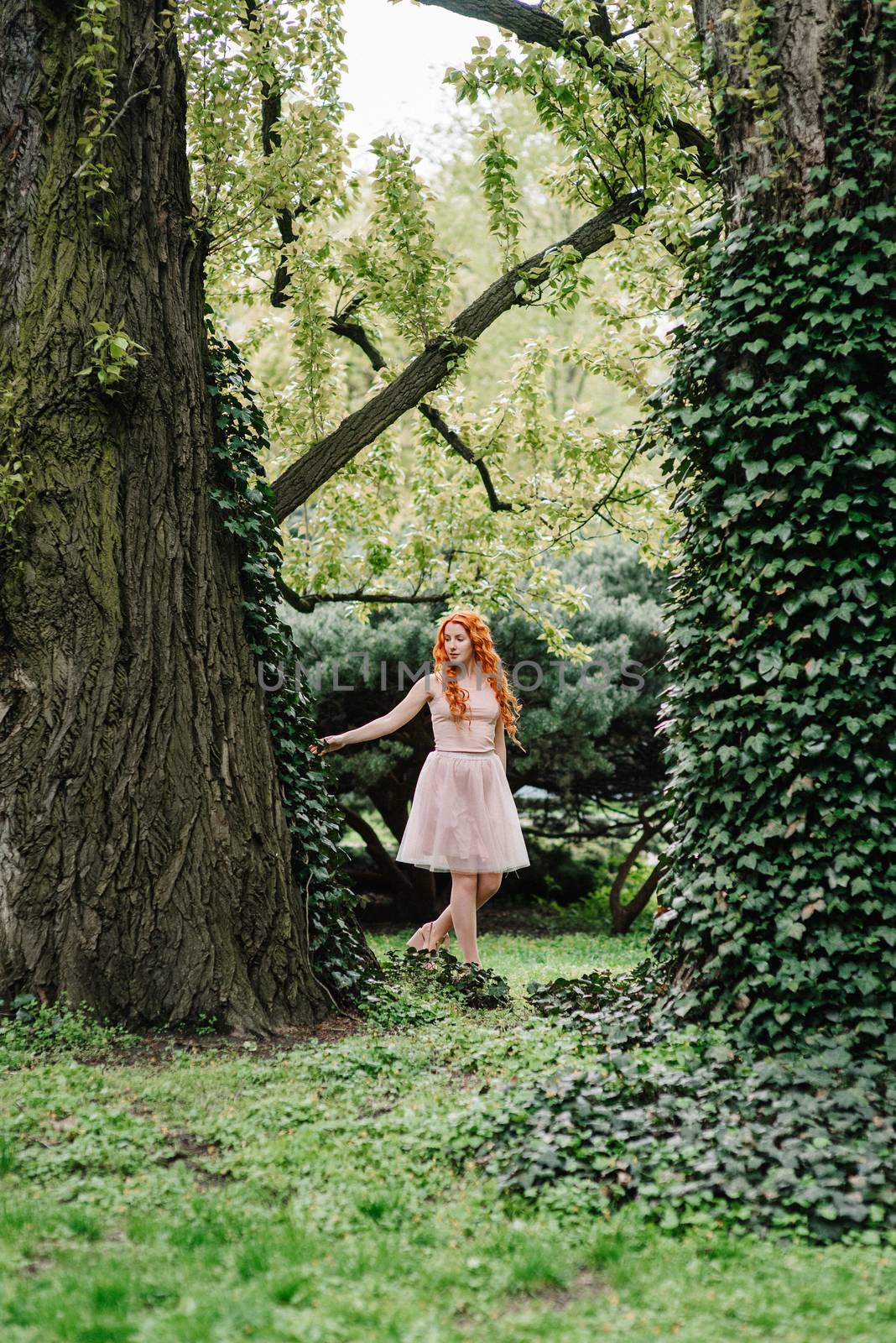 red-haired young girl walking in a park between trees by Andreua