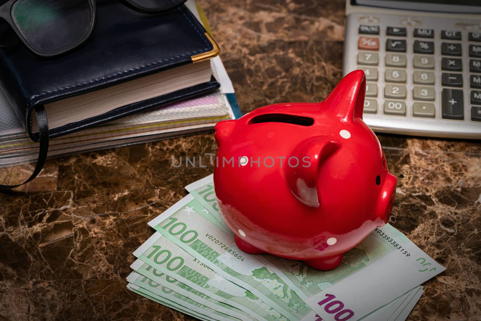 Emergency fund concept. Piggy Bank stands on Euro banknotes. Next to it is a diary and glasses.