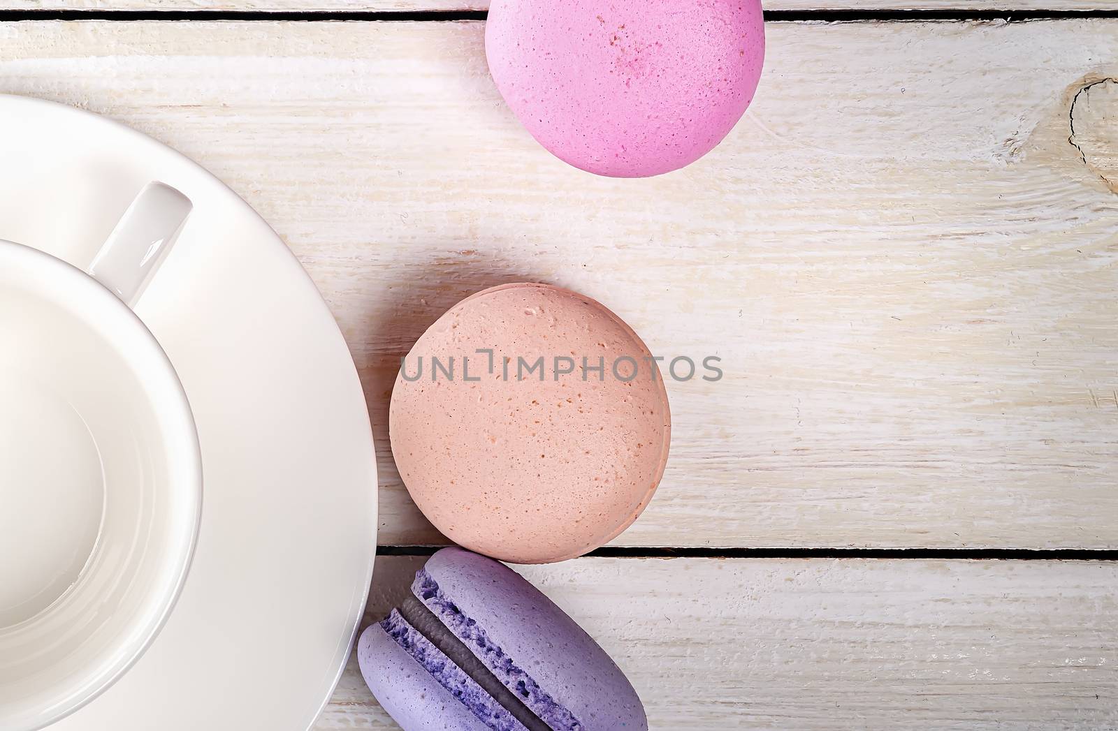 Multicolored macaroons near white coffee cup closeup top view on wooden table