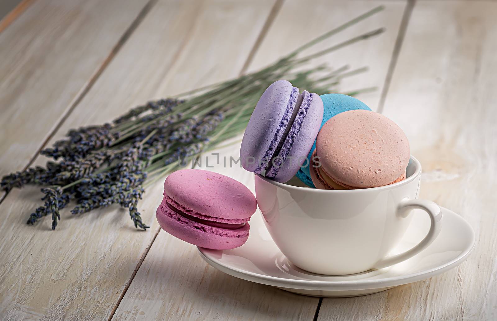 Multicolored macaroons in white cup with lavender on wooden table