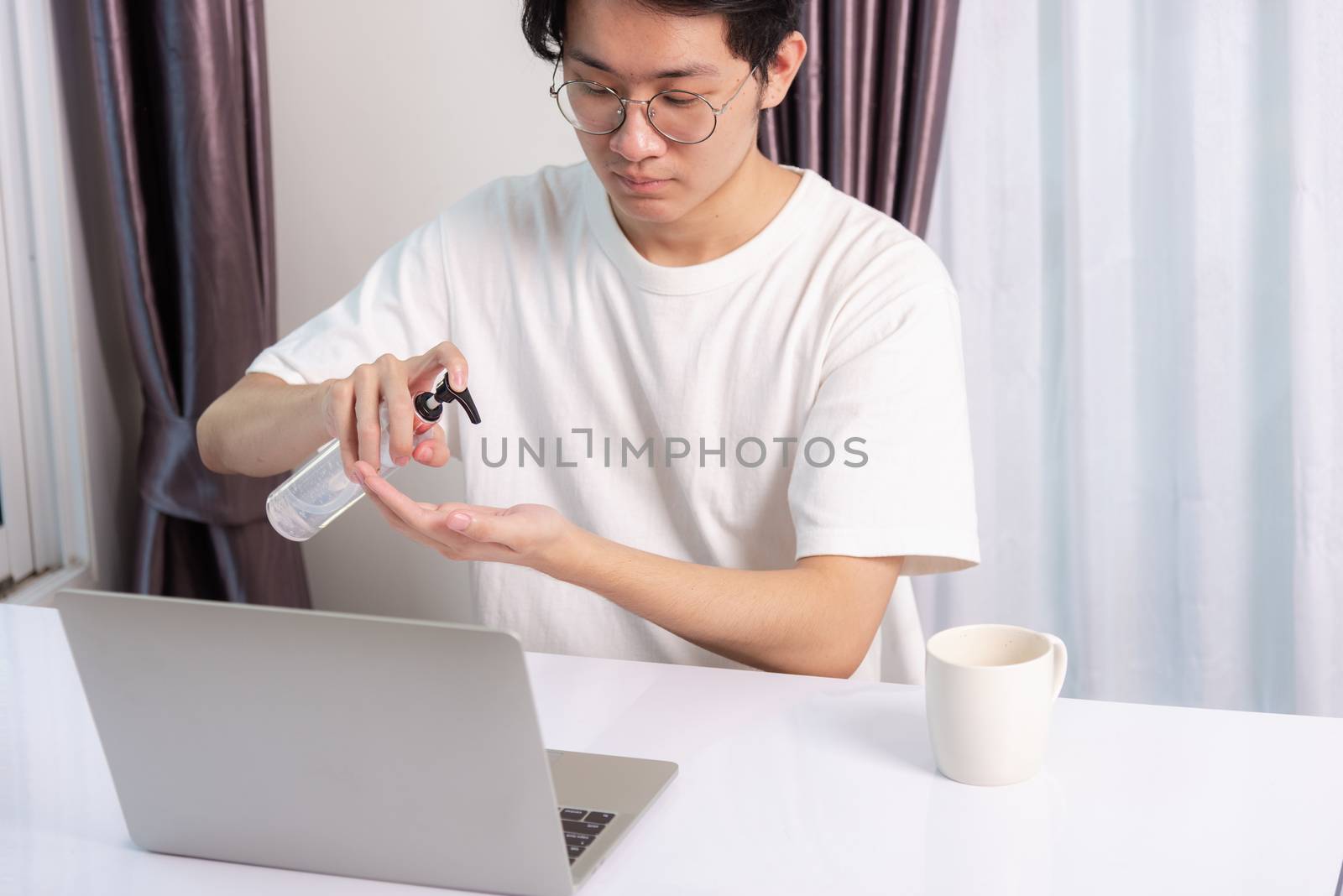 Asian business young handsome man glasses working from home office he quarantines disease coronavirus or COVID-19 wearing protective mask and cleaning hands with sanitizer gel on front laptop computer