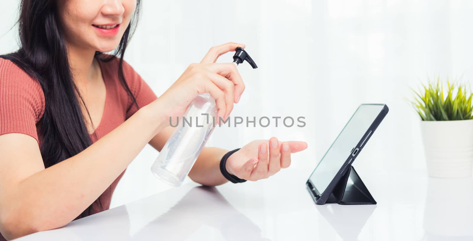 Asian Business young woman working from home office he quarantines disease coronavirus or COVID-19 her cleaning hands with sanitizer gel on front tablet computer