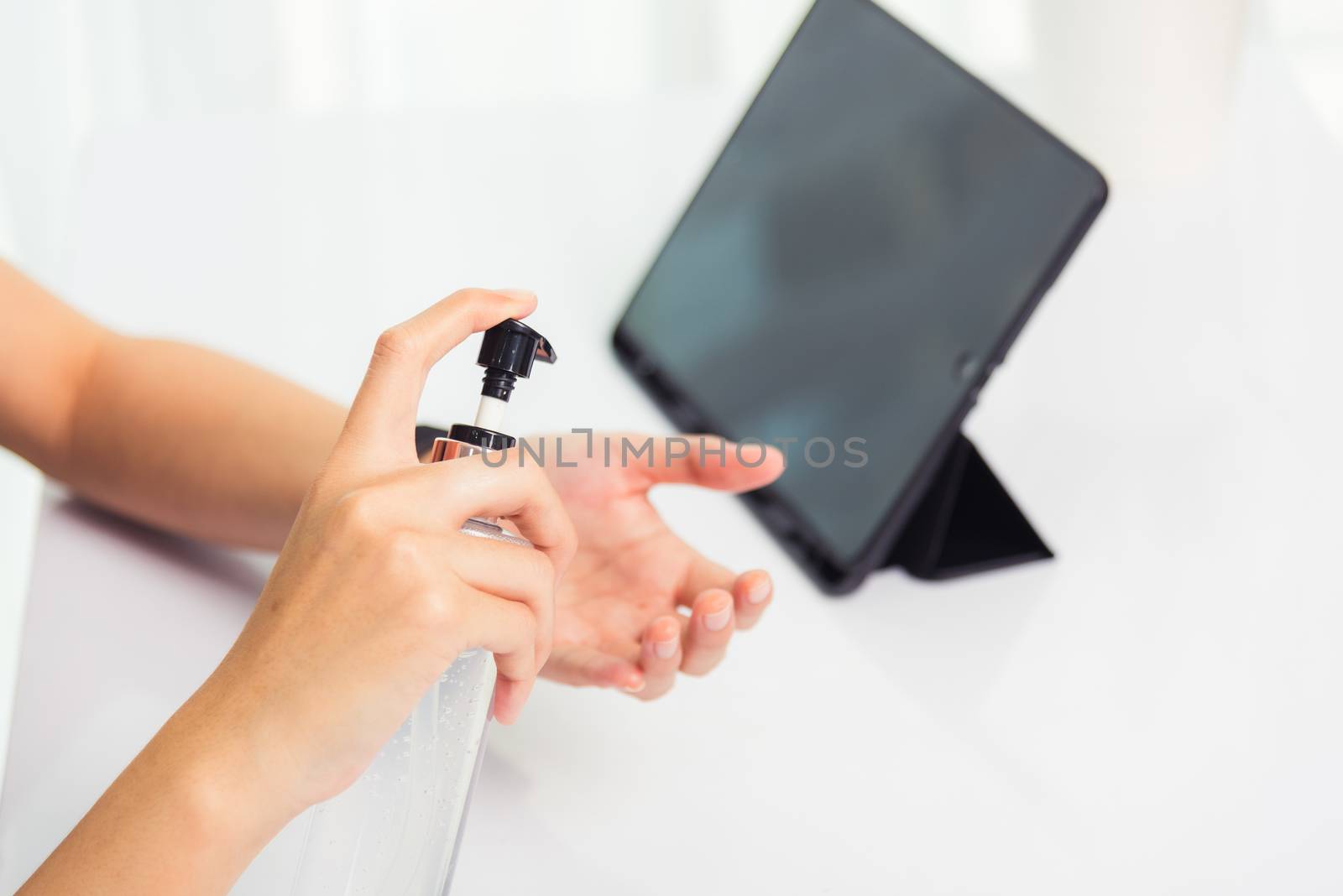 Asian Business young woman working from home office he quarantines disease coronavirus or COVID-19 wearing a protective mask and cleaning hands with sanitizer gel on front tablet computer