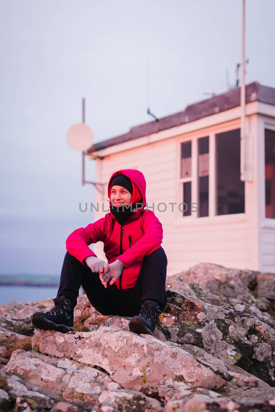 Woman sitting on the rocks watching the sunset at Martin's Haven Meteorological station in Wales, United Kingdom.