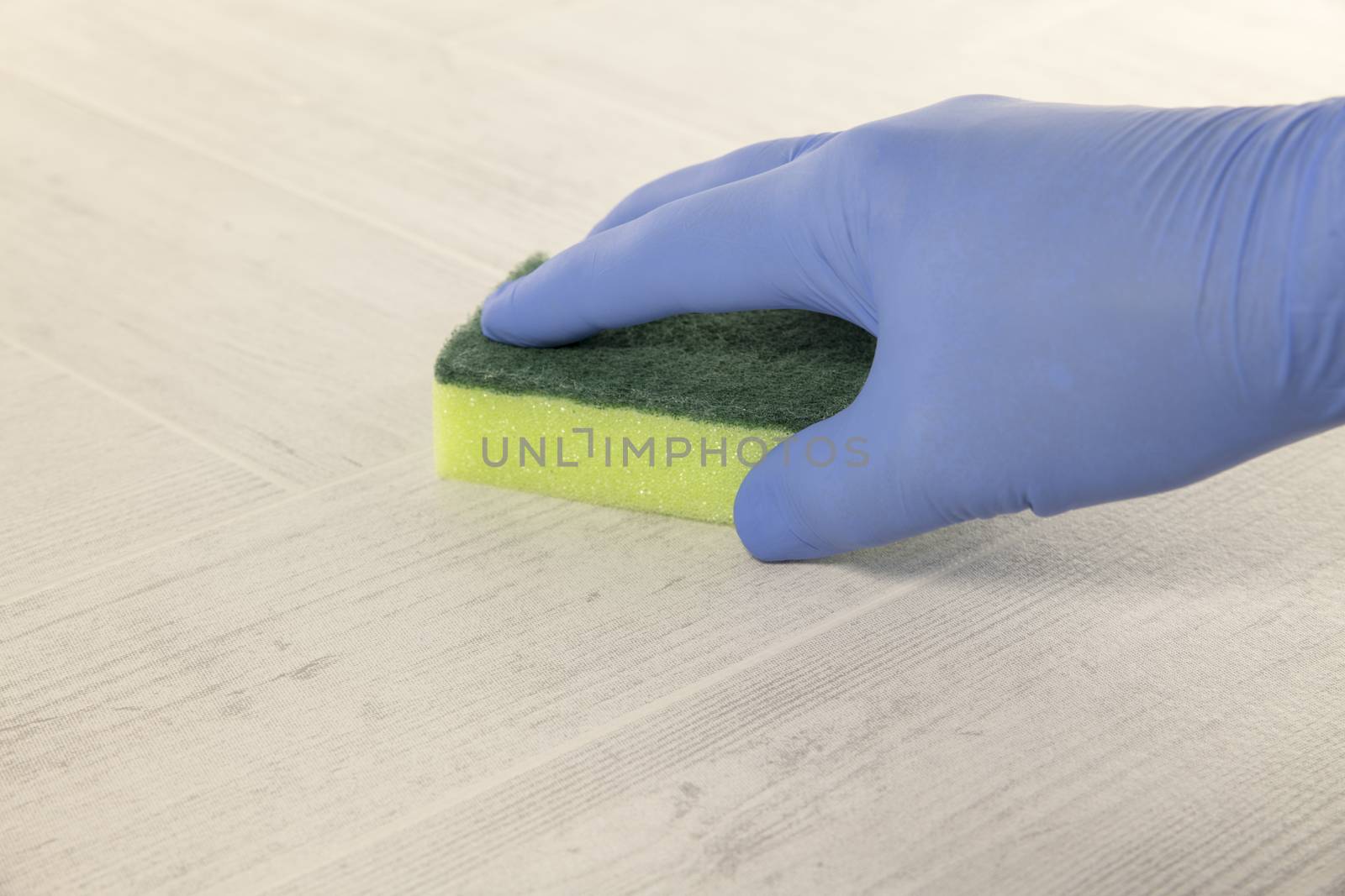 hand with blue rubber glove cleaning a floor with a green and yellow cleaning tool