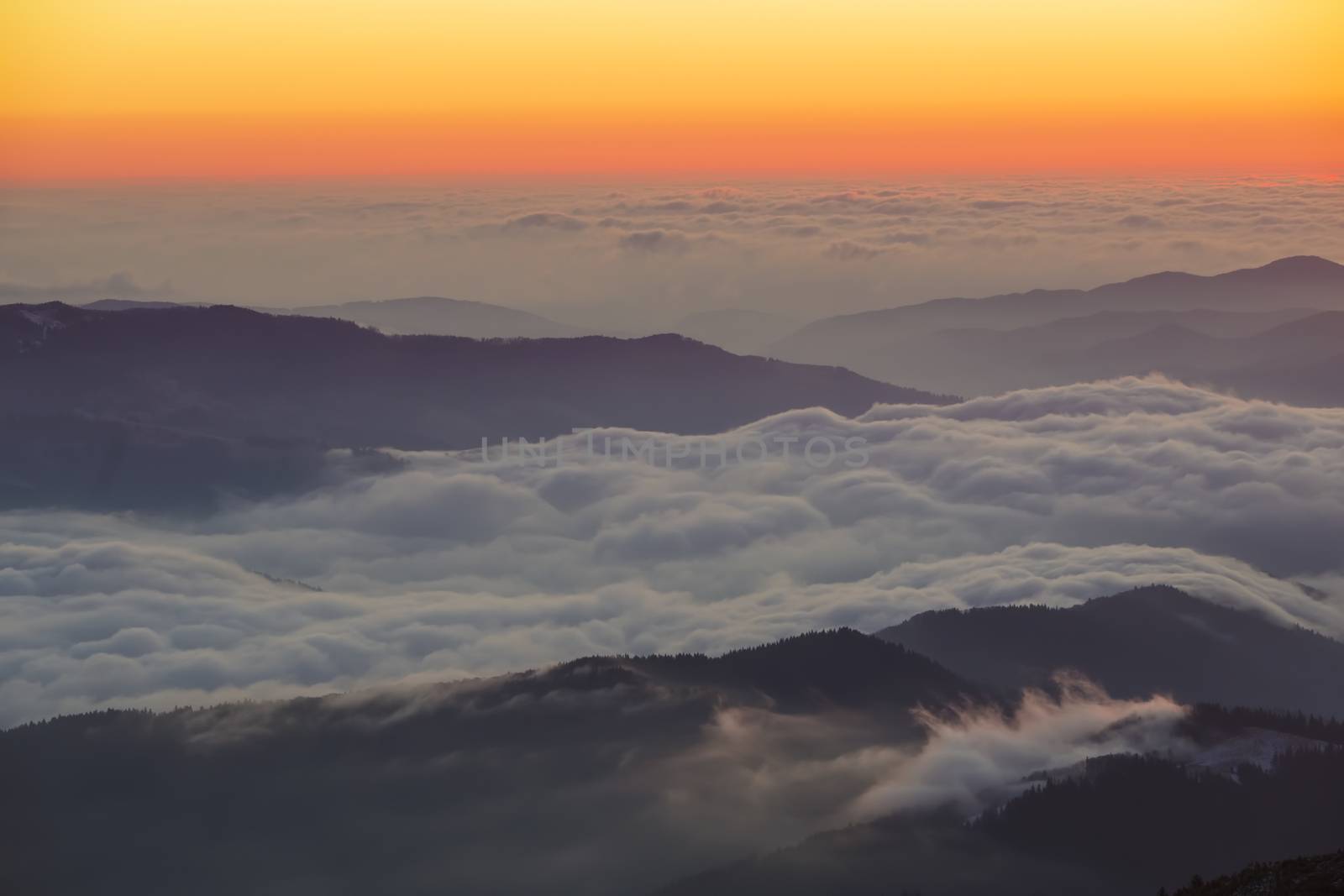 Beautiful sunrise landscape from mountain top in Romanian Carpathians. Low clouds on valley