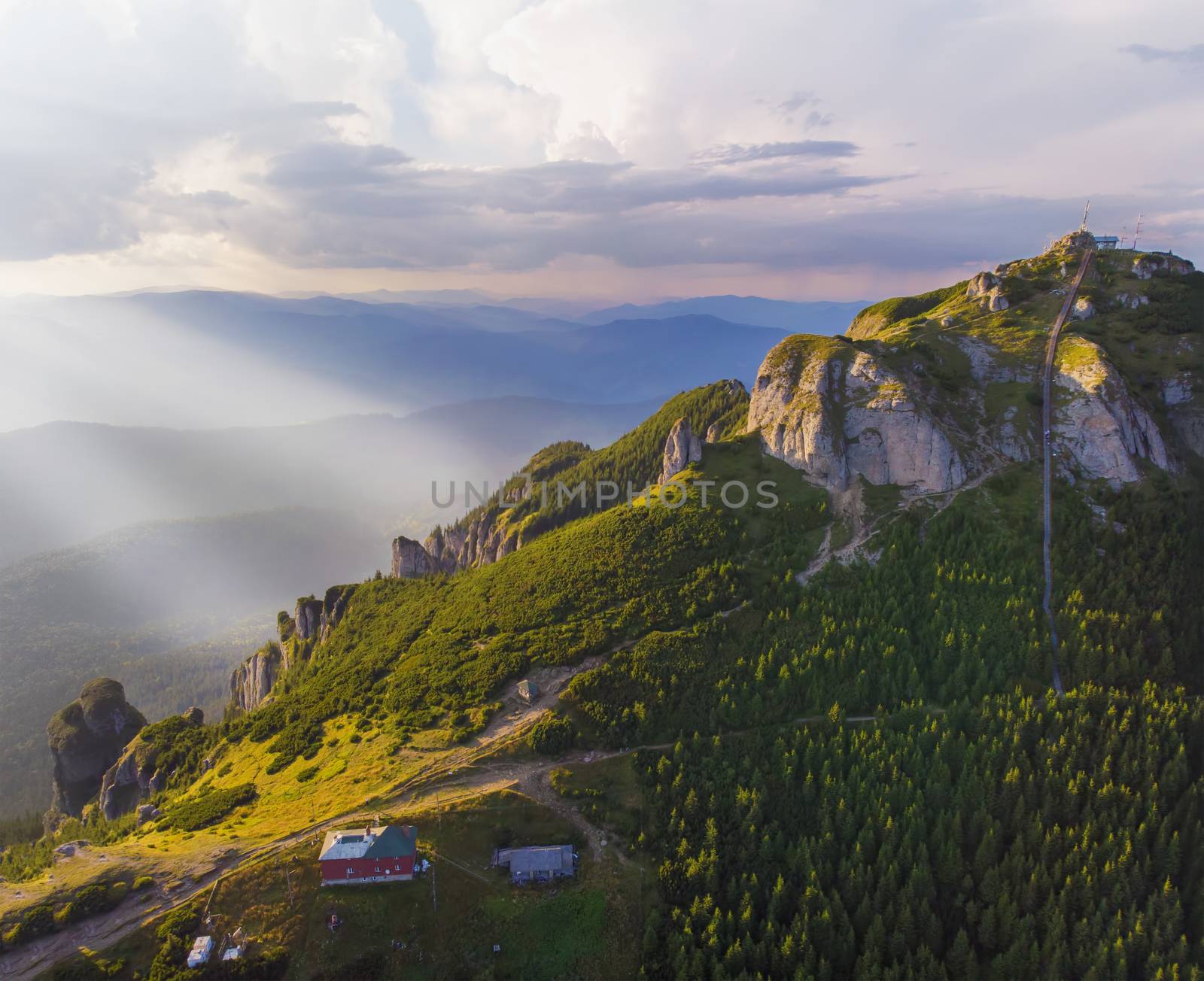 Sunset landscape from above, mountain chalet and rocky peak in Romanian Carpathians.