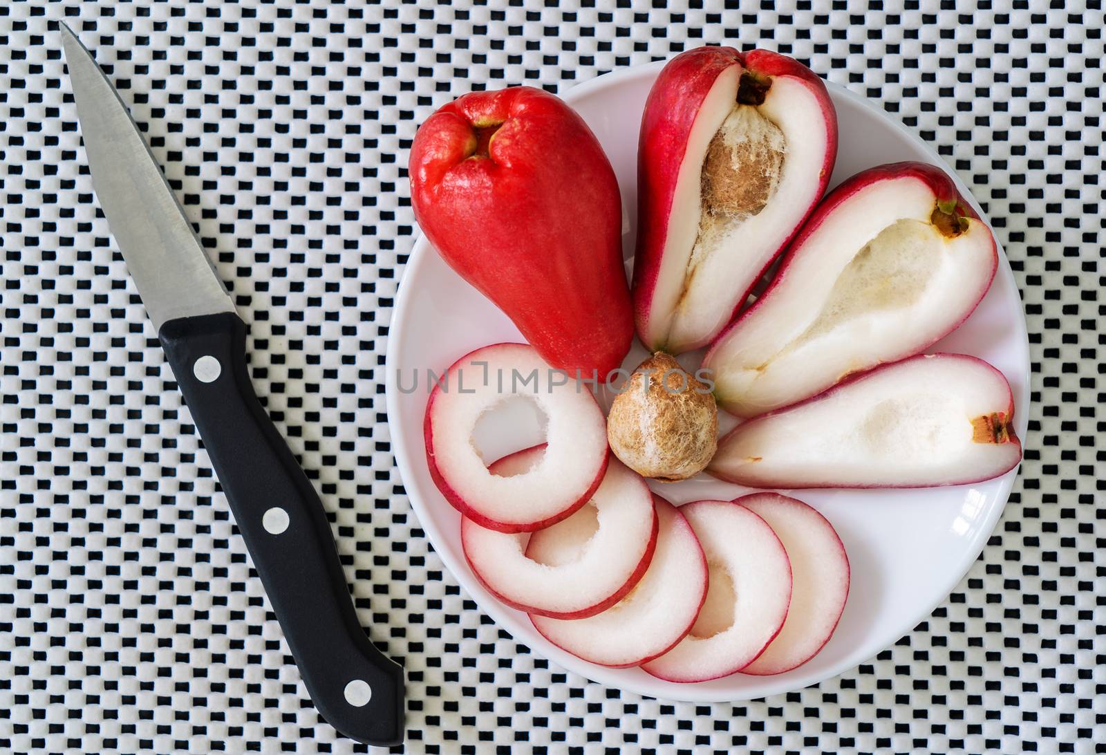 pieces of rose fruit in a plate on a white surface and a knife aside
