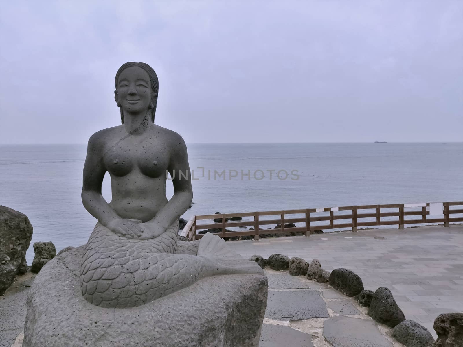 Mermaid statue made of black stone on the shore with sky and sea in south Korea