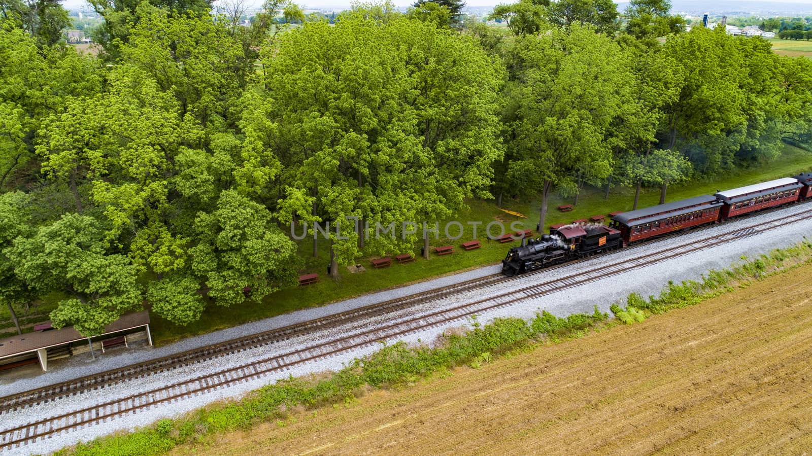 Ariel View of a Steam Passenger Train Pulling into Picnic Area Blowing Smoke on a Sunny Summer Day as seen by a Drone
