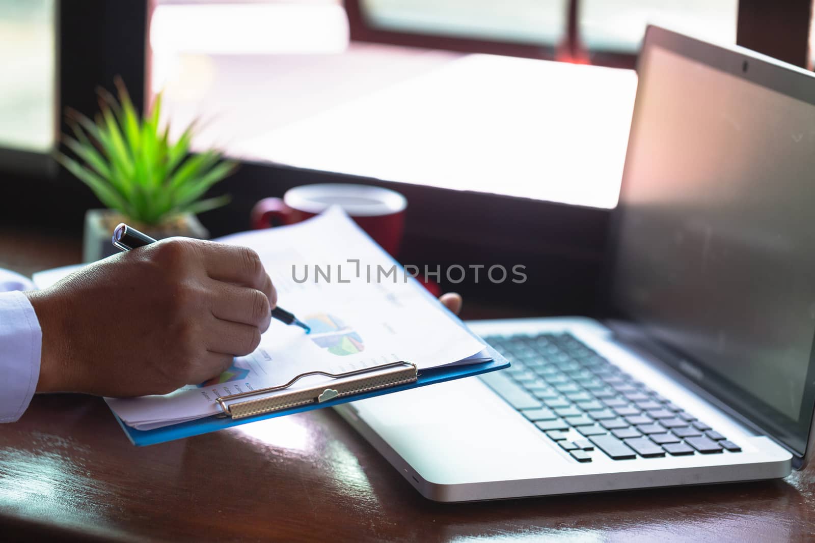 A business man sitting in front of a laptop, pointing pen, graphData analysis concept from summary graph statistics for business meeting executives.Graph, statistics, financial, management,accounting.