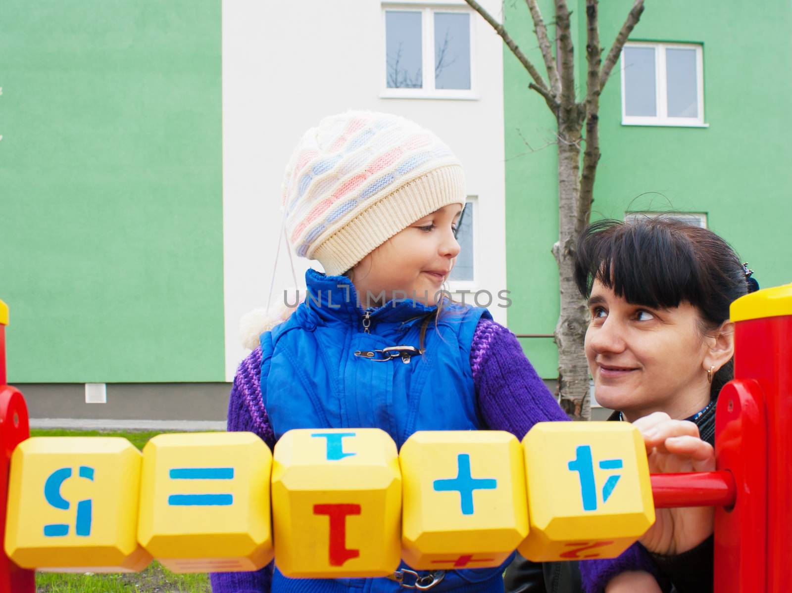 mom teaches daughter to be considered at the playground with wooden cubes on spring day outside
