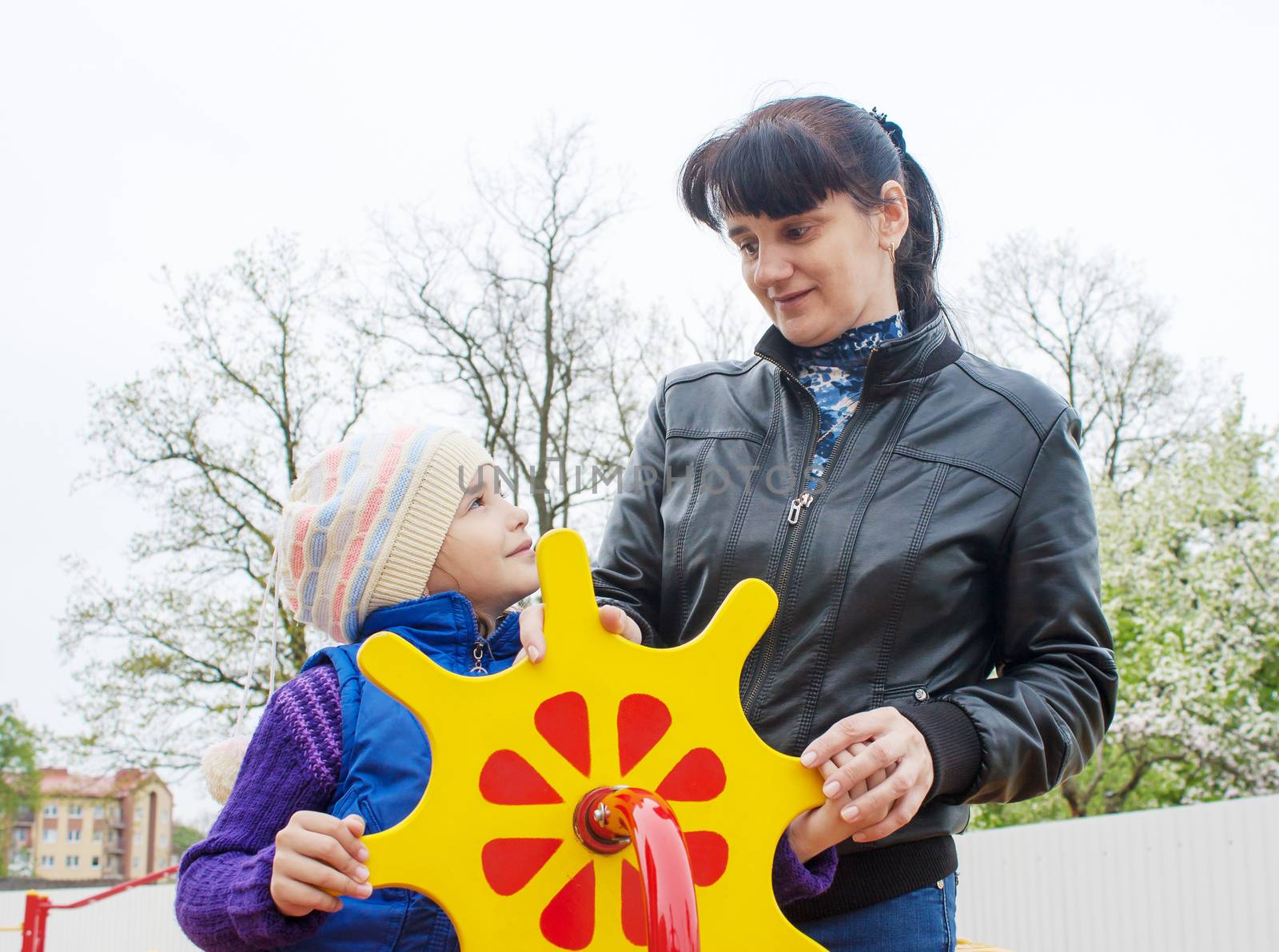 young mom plays with her daughter at the playground on a toy ship on spring day