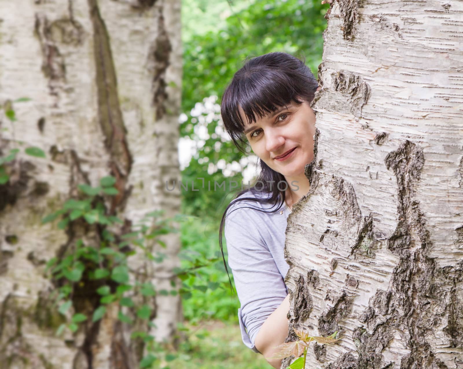 young beautiful smiling brunette woman looking out because of a birch