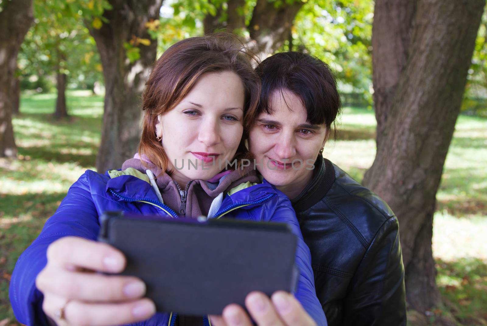 young woman with her mother taking pictures of themselves a mobile phone on autumn day outside