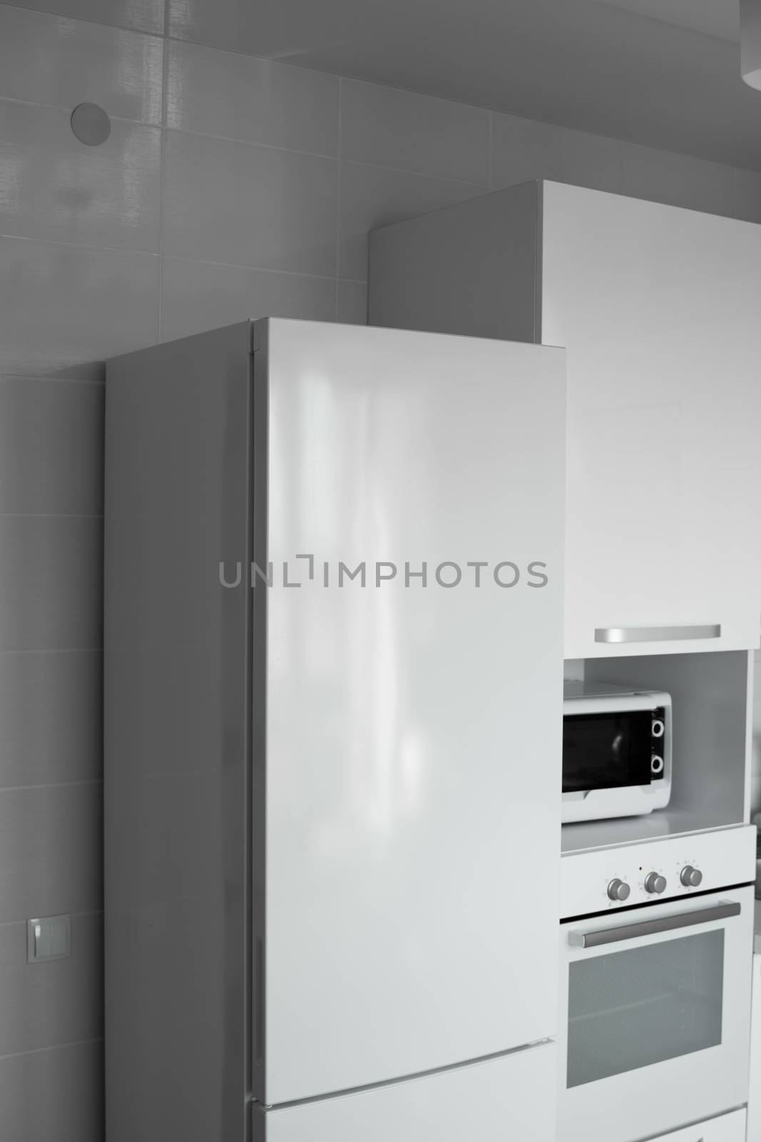 Comfortable white kitchen with a white lacquered facades. Modern kitchen clean interior design. Refrigerator, kitchen oven, microwave oven. Kitchen supplies