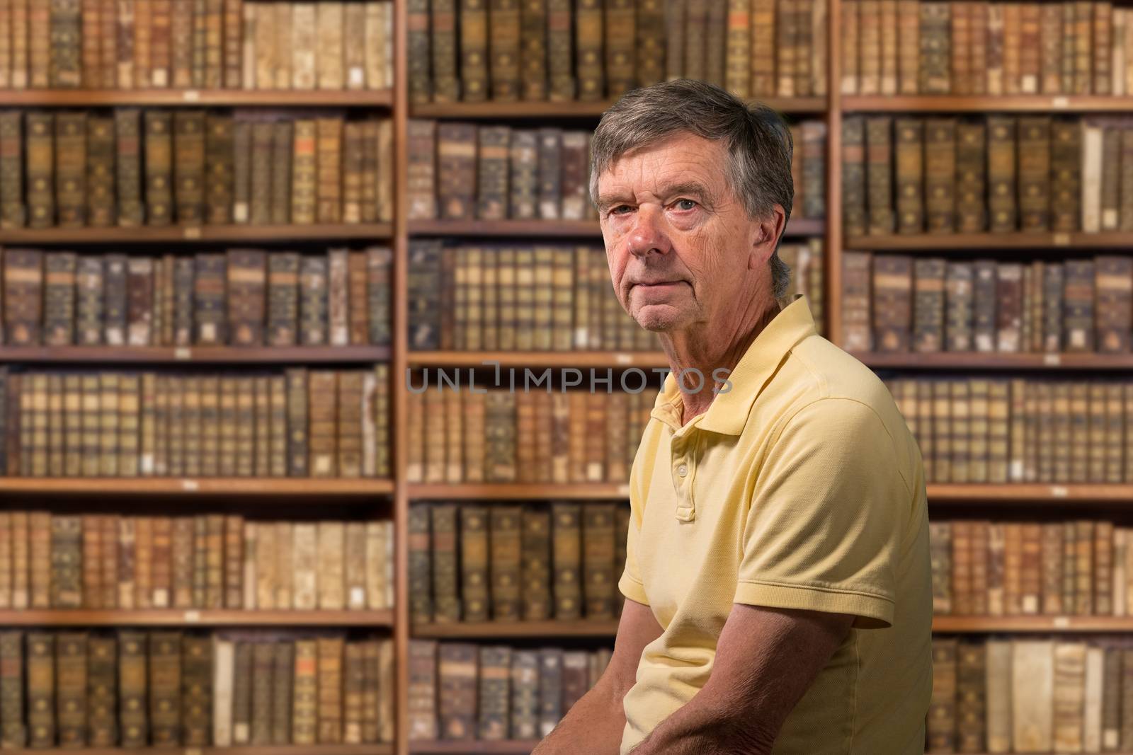Senior caucasian man sitting in library full of old books on shelves by steheap