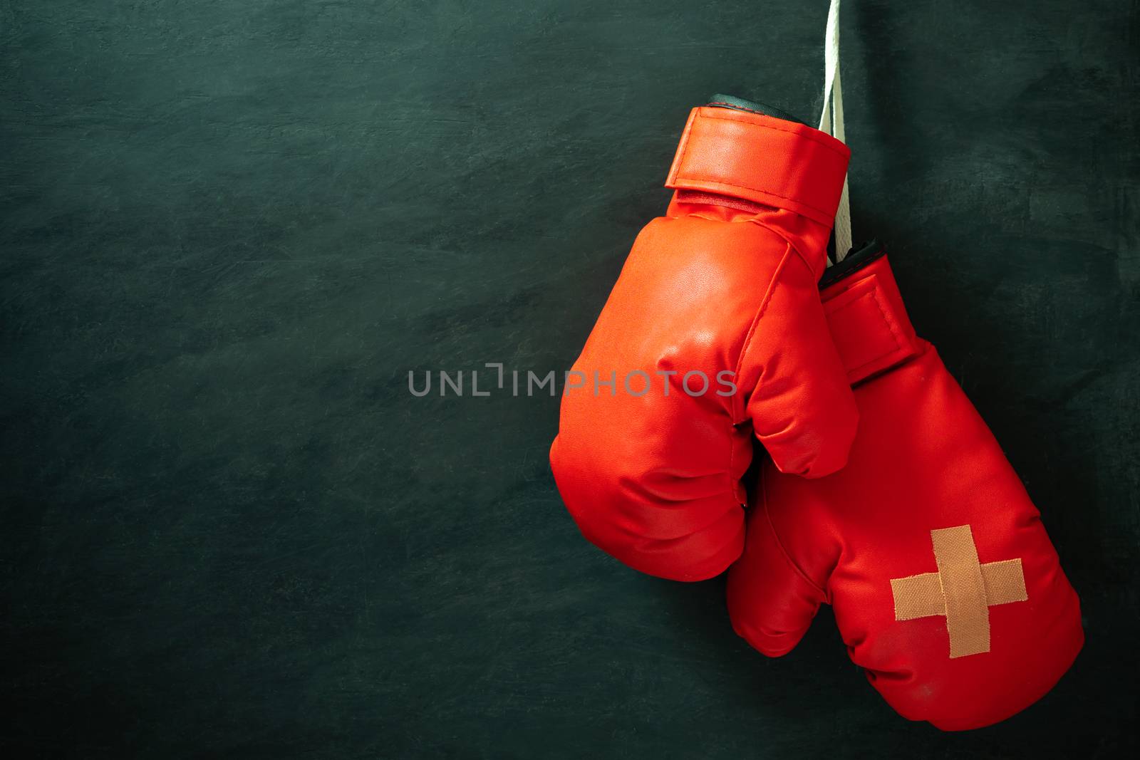 Red boxing gloves hung on black cement wall in darkness with lighting. Adhesive plaster across each other on boxing gloves. Idea of hurt or combat losing business rivals. Fighting giving up boxing.