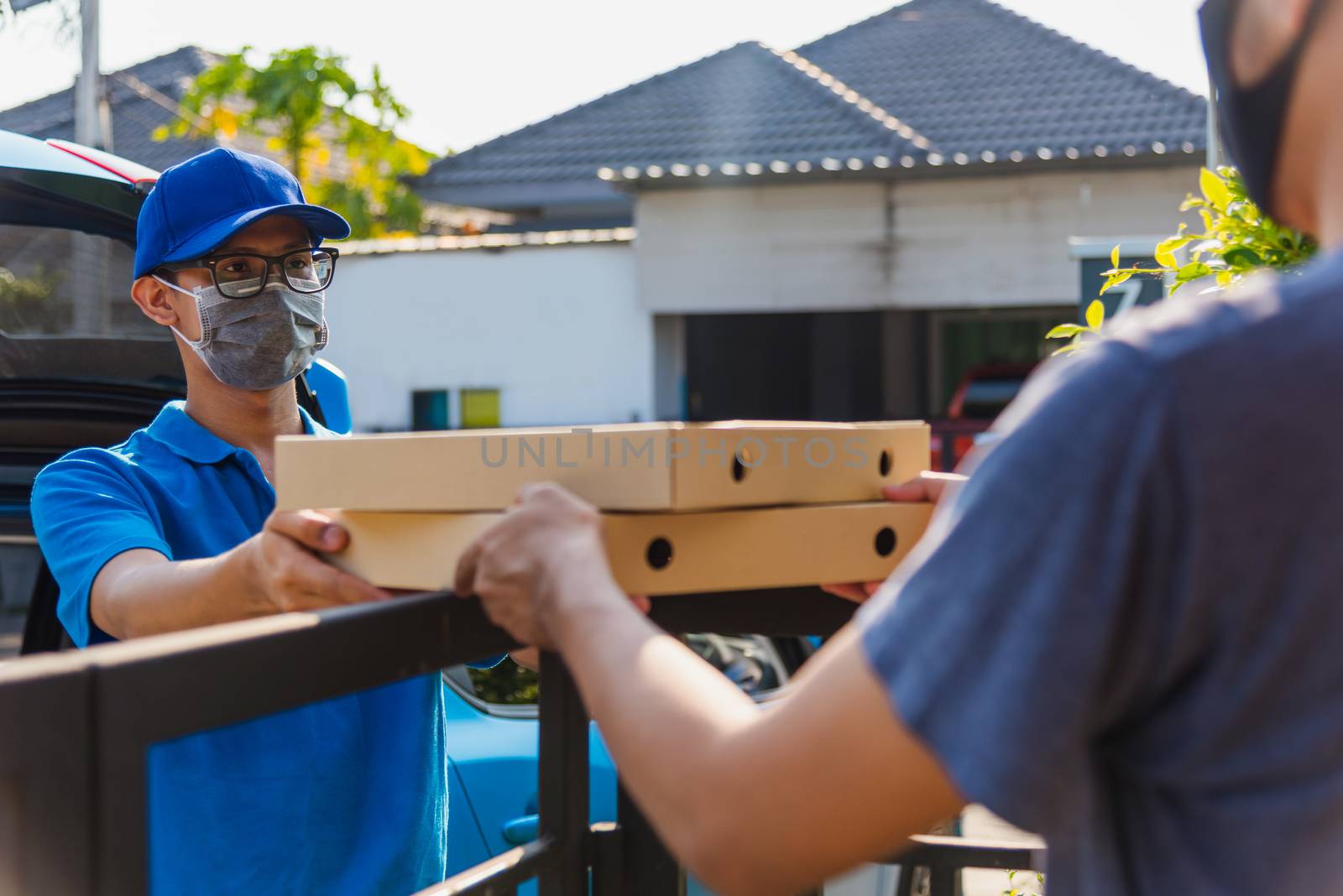 Asian delivery man courier online deliveries out pizza food boxes at home to customer her protective face mask service under curfew quarantine pandemic coronavirus COVID-19