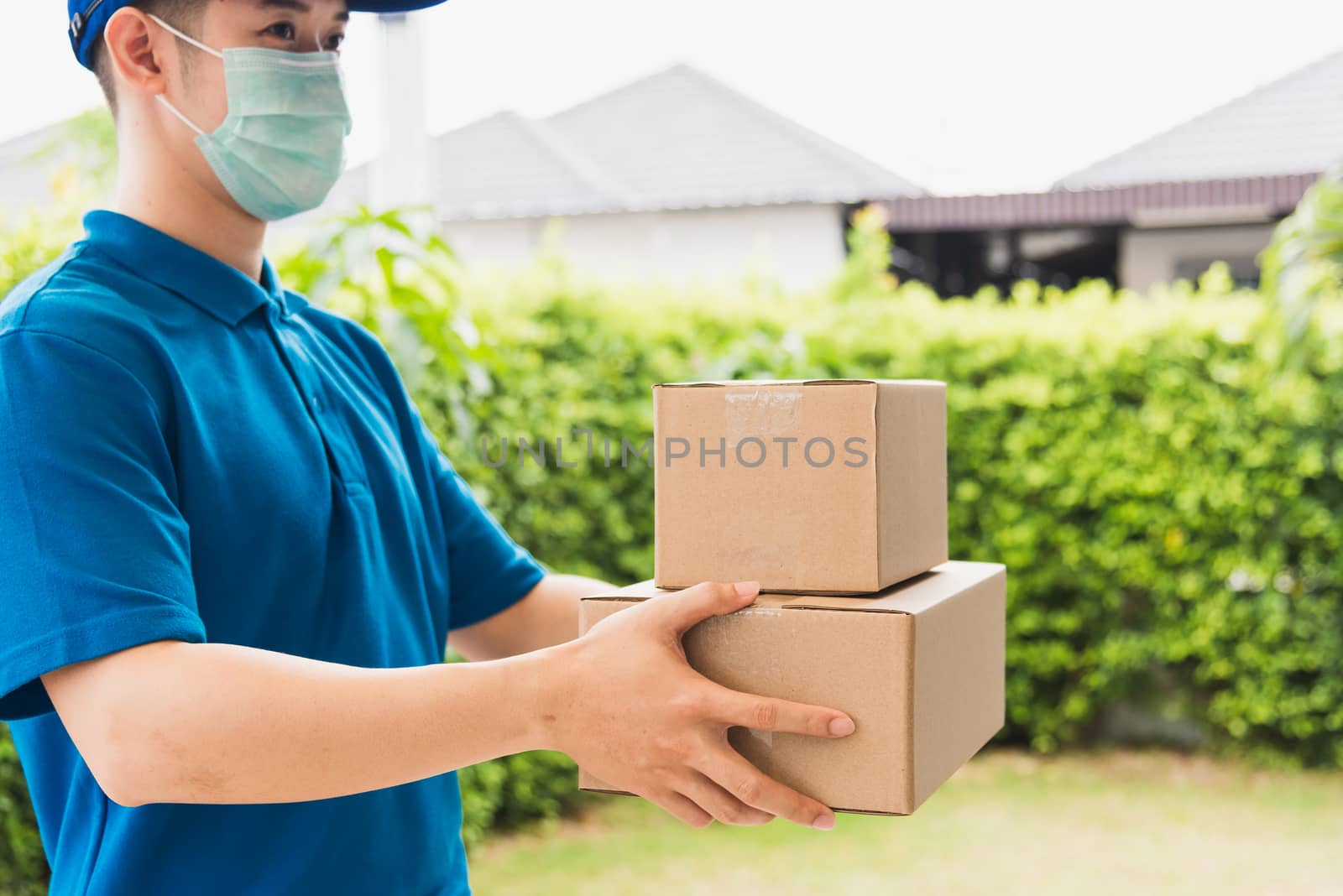 Asian delivery express courier young man use giving boxes to woman customer he wearing protective face mask at front home, under curfew quarantine pandemic coronavirus COVID-19