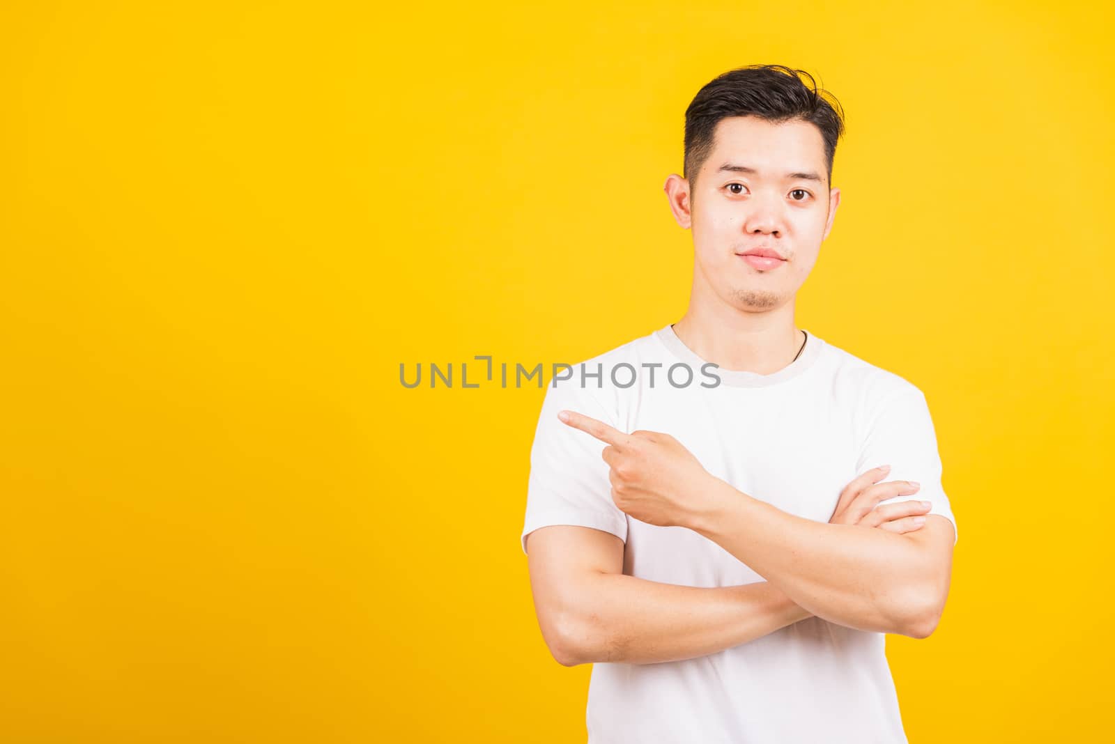 Portrait happy Asian handsome young man smiling standing wearing white t-shirt pointing finger to the side away he looking to camera, studio shot isolated yellow background